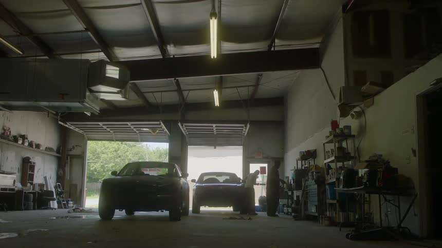 Two men stand near cars parked in a large garage