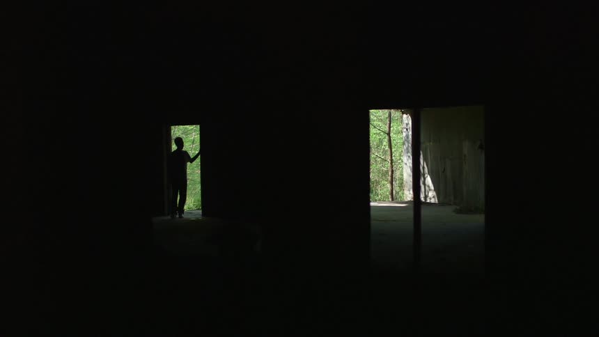 A young male is walking into an abandoned building through a doorway with no door