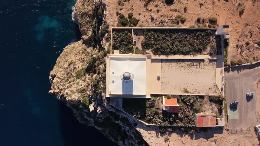 Aerial view shows a building on a cliff by the sea with an adjacent road