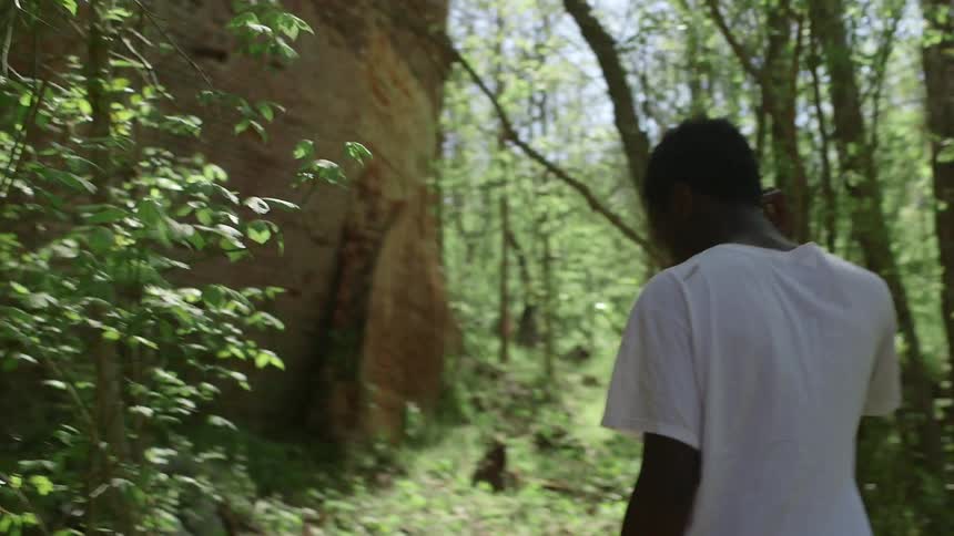 A teenage boy is walking toward an abandoned building in an area overgrown with vegetation