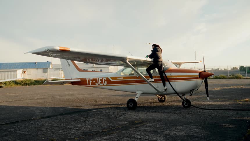 Woman standing on the side of a small airplane with her hands on the wing