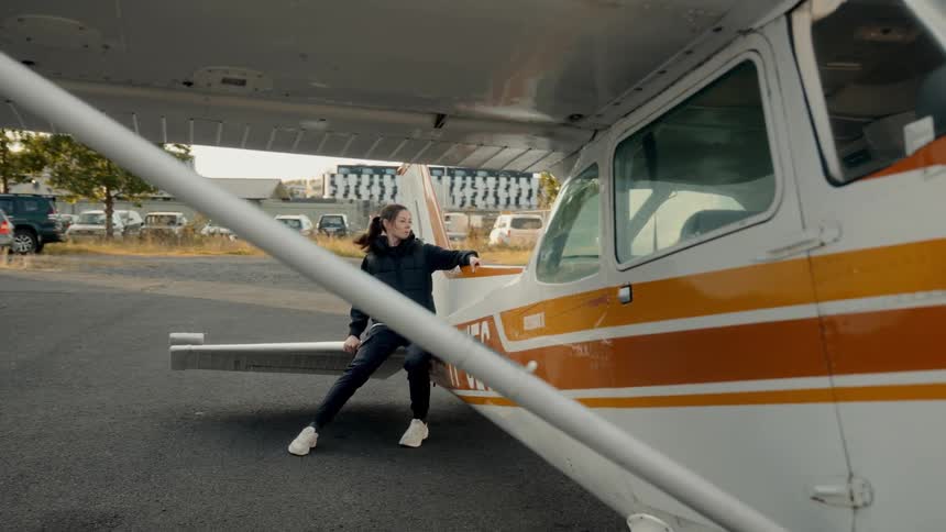 Woman holding the door of a small airplane under the wing in an outdoor area