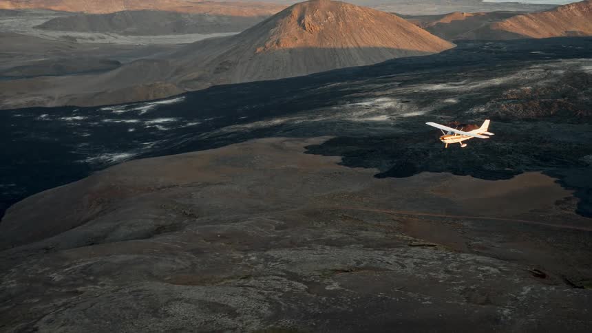 A small single propeller airplane flies over a mountainous landscape