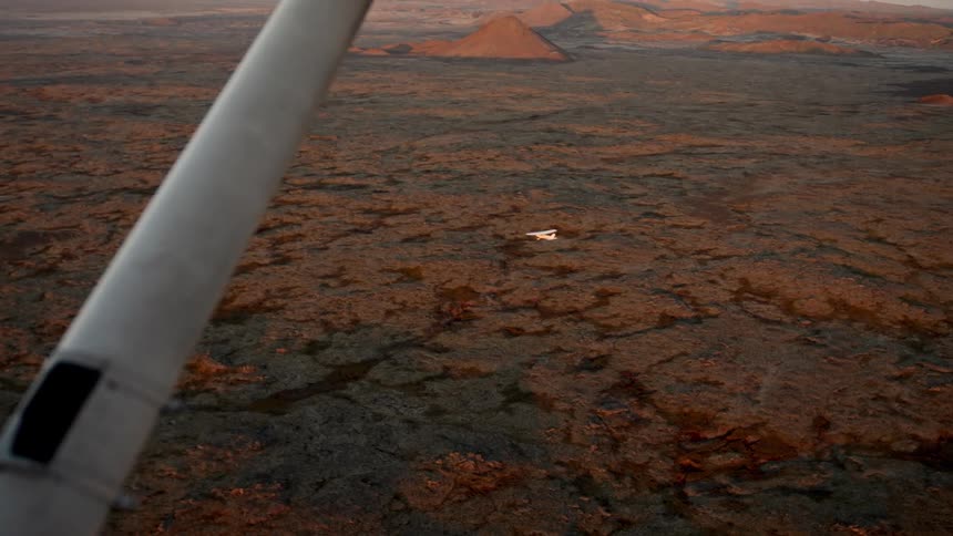 Aerial view of arid cracked ground with aircraft wing visible in low flight