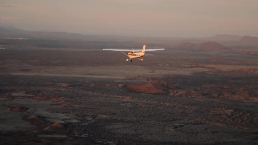 Airplane flying over a badlands landscape with mountains on the background outdoors during dusk or dawn