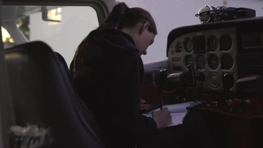 A young woman sitting on an airplane writing a note