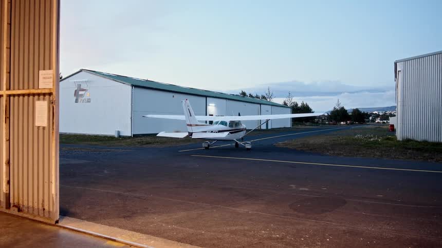 Airplane sits between hangars near a brightly lit hangar on a cloudy day