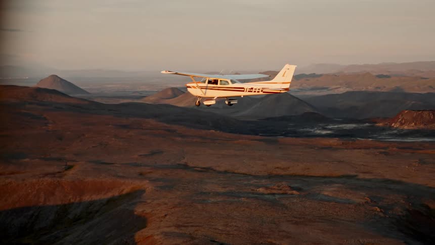 Small plane flies over hilly terrain on a foggy day