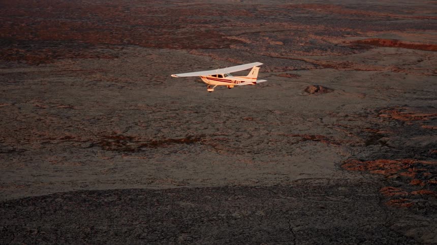An aircraft flying over rocky terrain at sunset