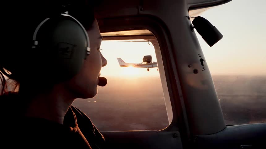Person wearing a headset watches another airplane through the window at sunset
