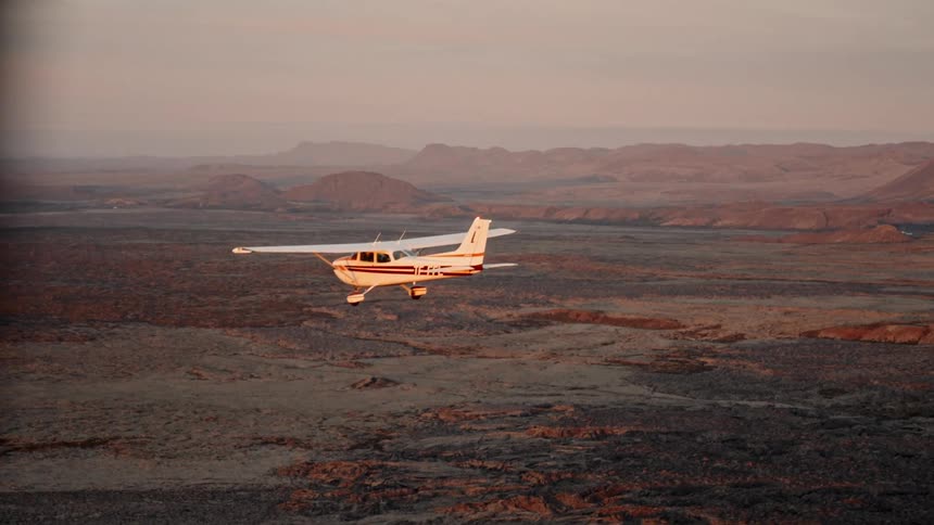 One small aircraft parallels another as they fly over rough terrain on a foggy day