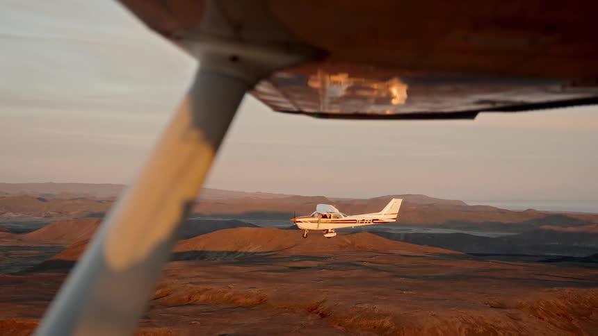 Singleengine airplane flying over a canyon in a desert landscape seen from the structure of another aircraft at sunset