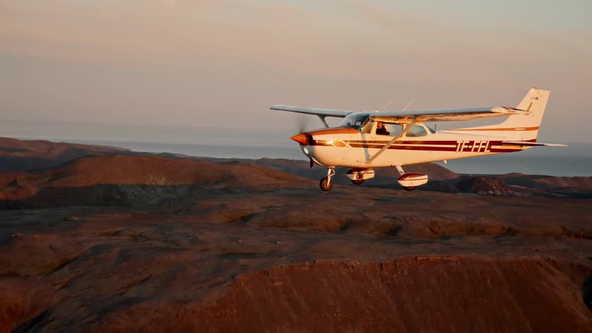 Small airplane flies over hilly terrain under a cloudy sky