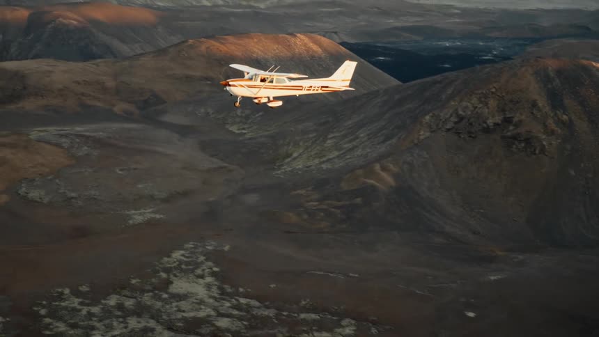 Singleengine airplane flies over mountainous terrain with the ocean in the background