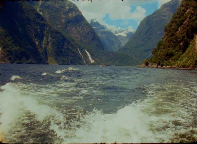 Waves formed by a boat on a lake between mountains with a waterfall in the background