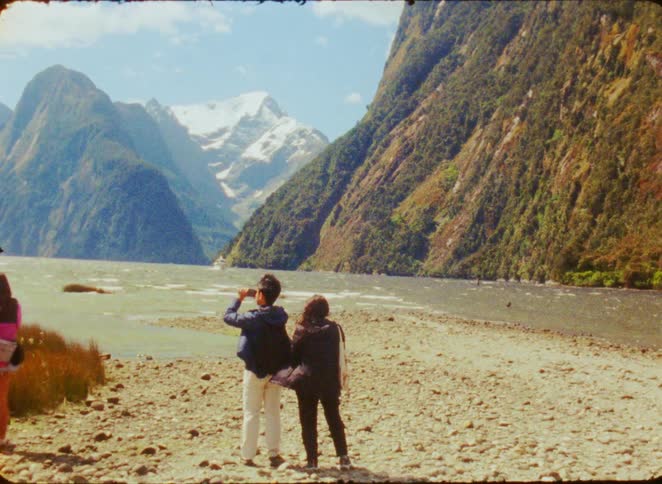 A young couple admires the massive snowcapped mountains from the shoreline