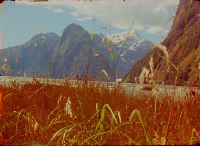 Lush foreground grass frames majestic mountains and a tranquil water body