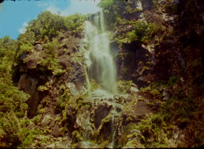 Waterfall flows down a rocky cliff covered with vegetation