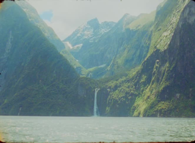 Waterfall descends between green mountains into a wide lake