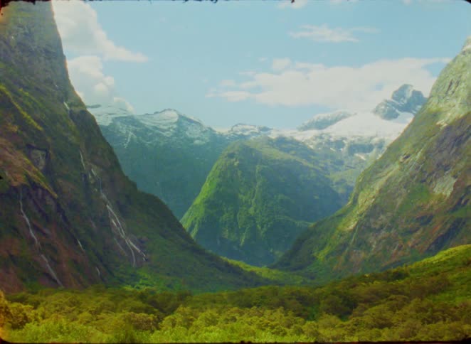 Majestic snow capped mountains rise above lush green valleys under a clear sky