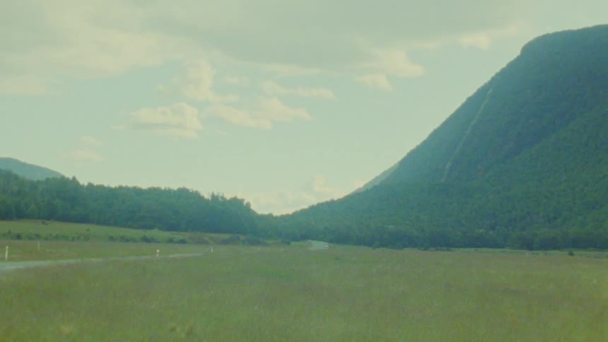 A rural road runs through a grassland near a green mountain