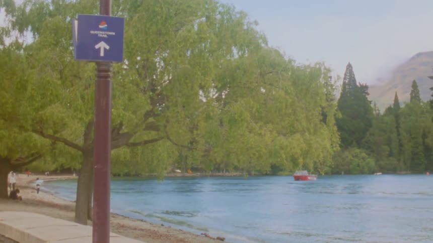 Sign indicates direction to a trail along a lakeshore with a boat in the background