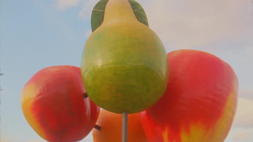 Giant sculpture of colorful fruits mounted on a metal structure outdoors against the sky