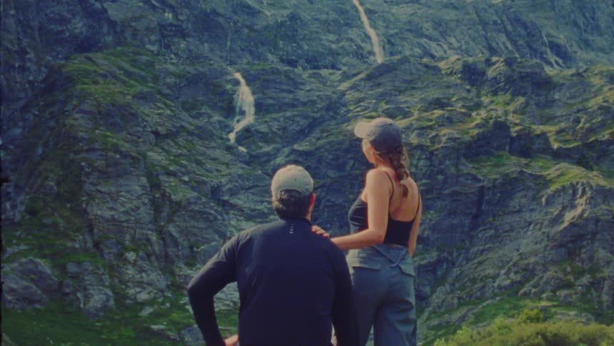 Couple looks at a rocky mountain with waterfalls in the background