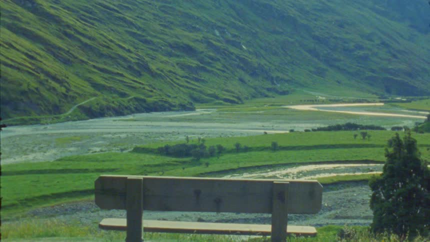 A wide grassland with a mountain covered in grass and a wooden bench on a hill