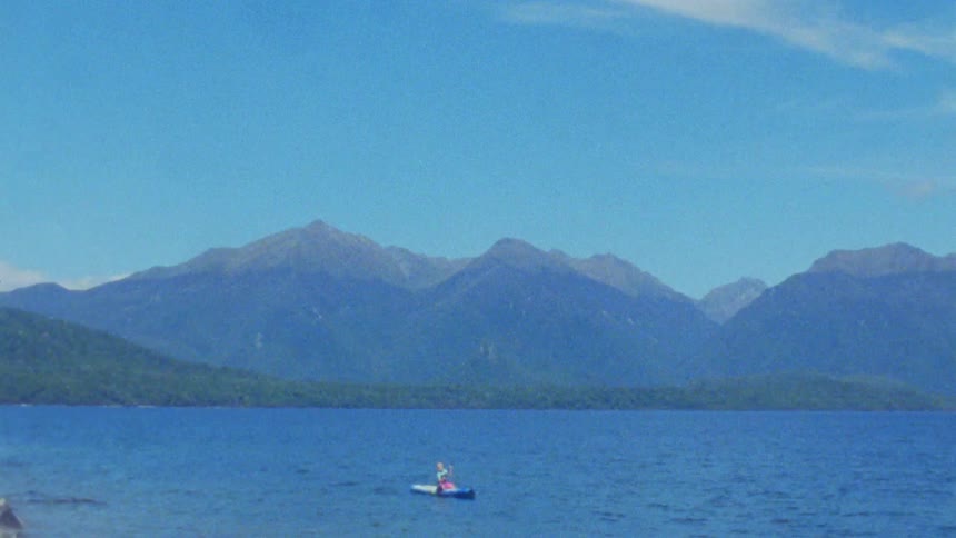 Person in small boat on blue lake with mountains in background under clear sky