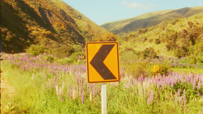 A natural resrve with an arrow direction sign pointing to the left side with grasses and hills across the land