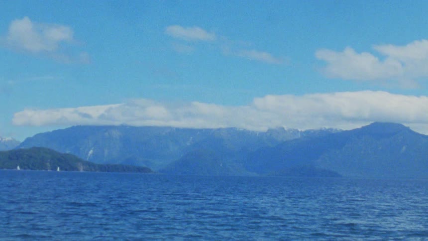 A lake surrounded by mountains with white clouds covering the sky at midday