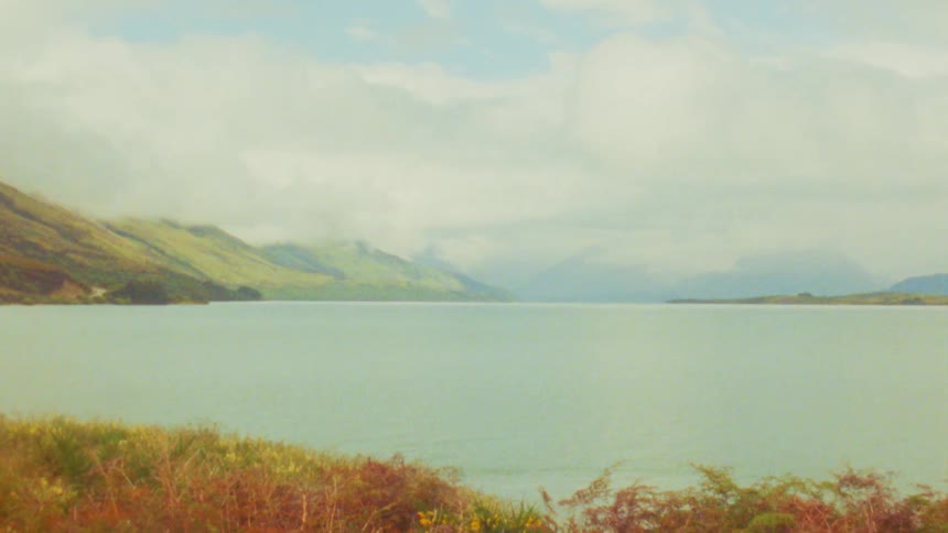 A lake view with a mountain range in the background surrounded by brown grasses from fall under a cloudy sky