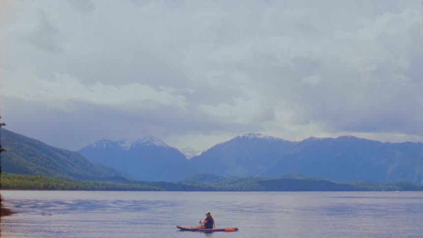 Person gets up and sits on a paddleboard in scenic mountain lake