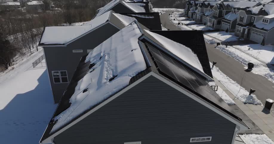 An aerial view shows solar panels on the roof of a grey house in a suburban neighborhood during a sunny day at winter