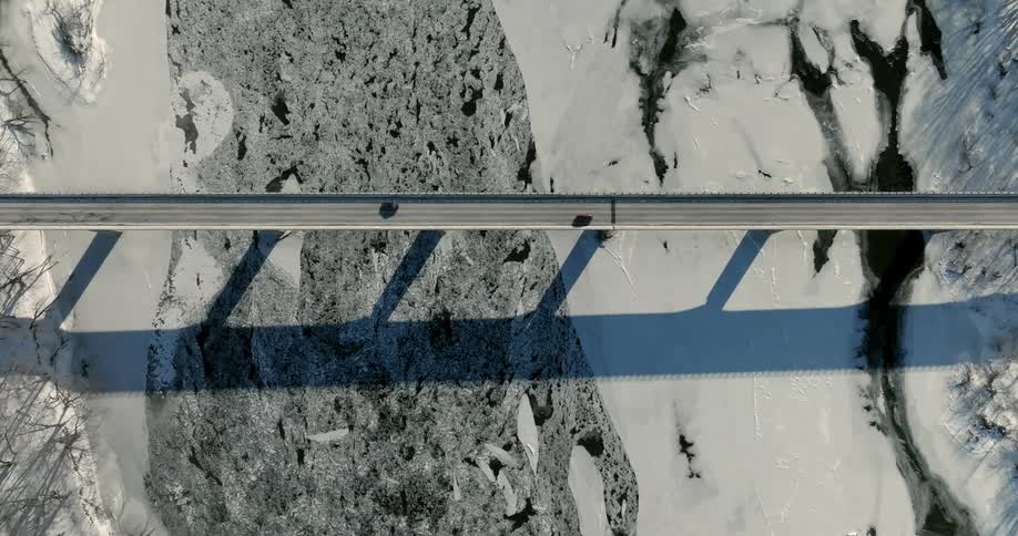 An aerial view shows cars driving across a bridge over a river filled with chunks of ice and snow during the day