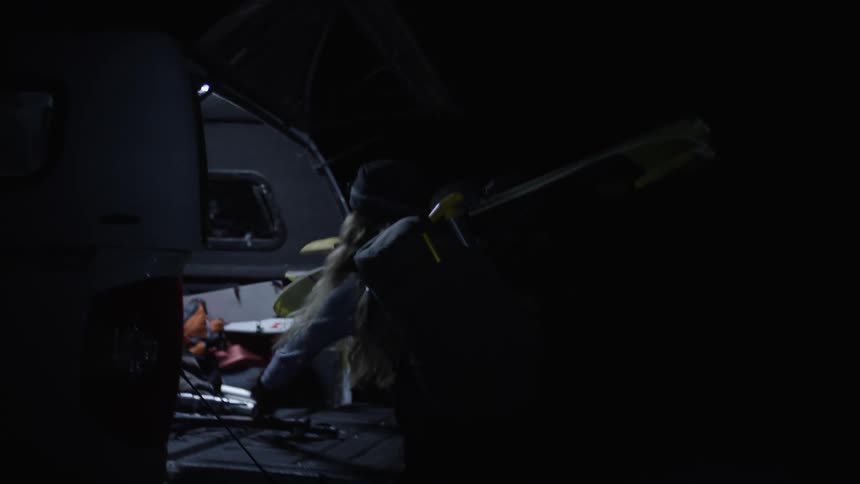 Man and woman removing ski equipment from the back of a vehicle at night