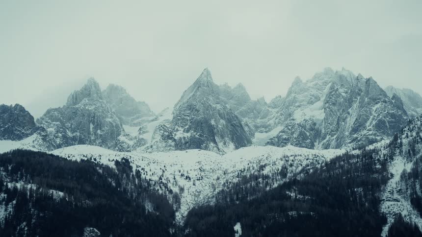 Snow covered forested mountains under a cloudy winter sky