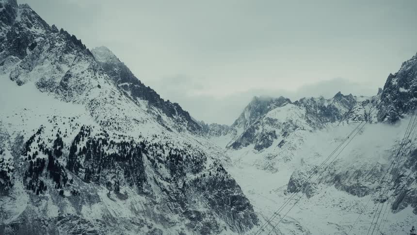Snow covering the rough terrain of mountains under a cloudy winter sky