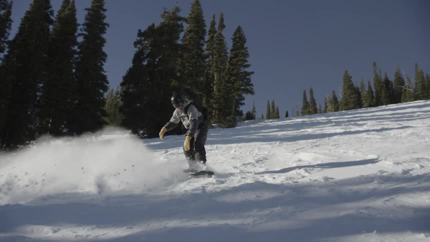 Snowboarder keeps his balance sliding down a snow covered mountain slope