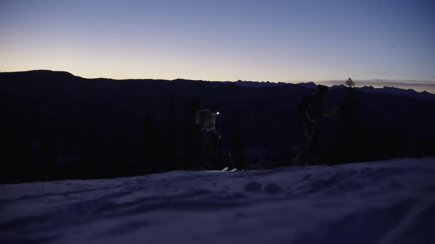 Skier in motion on snowy slope at dawn with mountains in the background