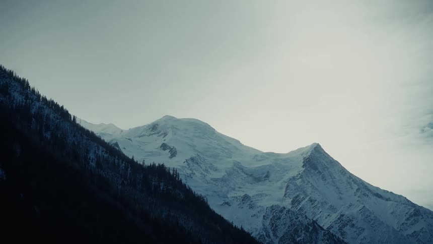 A mountain view with a snowcovered peak in the winter evening and a nearby mountain covered in short grasses