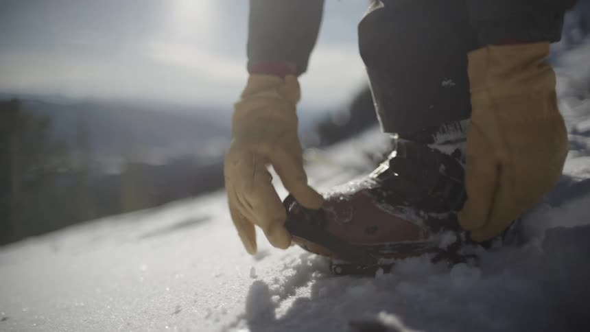 Person with yellow gloves fastening snowshoe in snowy setting