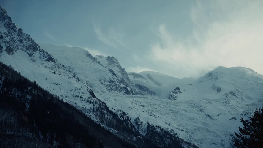 Snow and ice covers the rough terrain of mountains with trees and vegetation