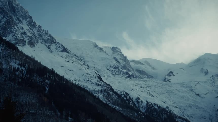 Snow covered forested mountains under a cloudy sky
