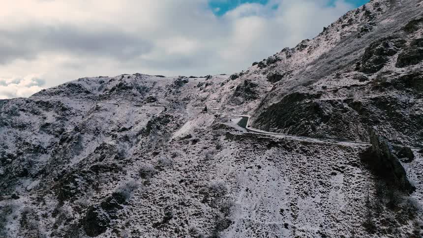 Winding road crosses snowcovered mountains under a partly cloudy sky