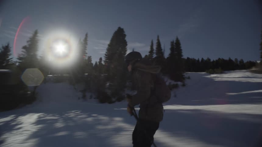 People skiing down a snow covered mountain as sunlight shines and hides behind trees