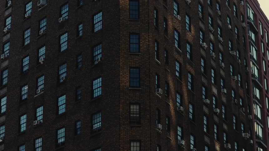 A view of a brown brick building with many windows and air units during the day
