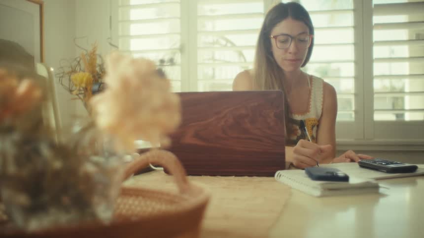 Teenage girl sitting at a table with a laptop computer and writing in a notebook