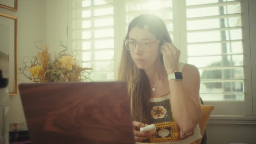 Woman puts on an earbud while using a laptop seated at a table
